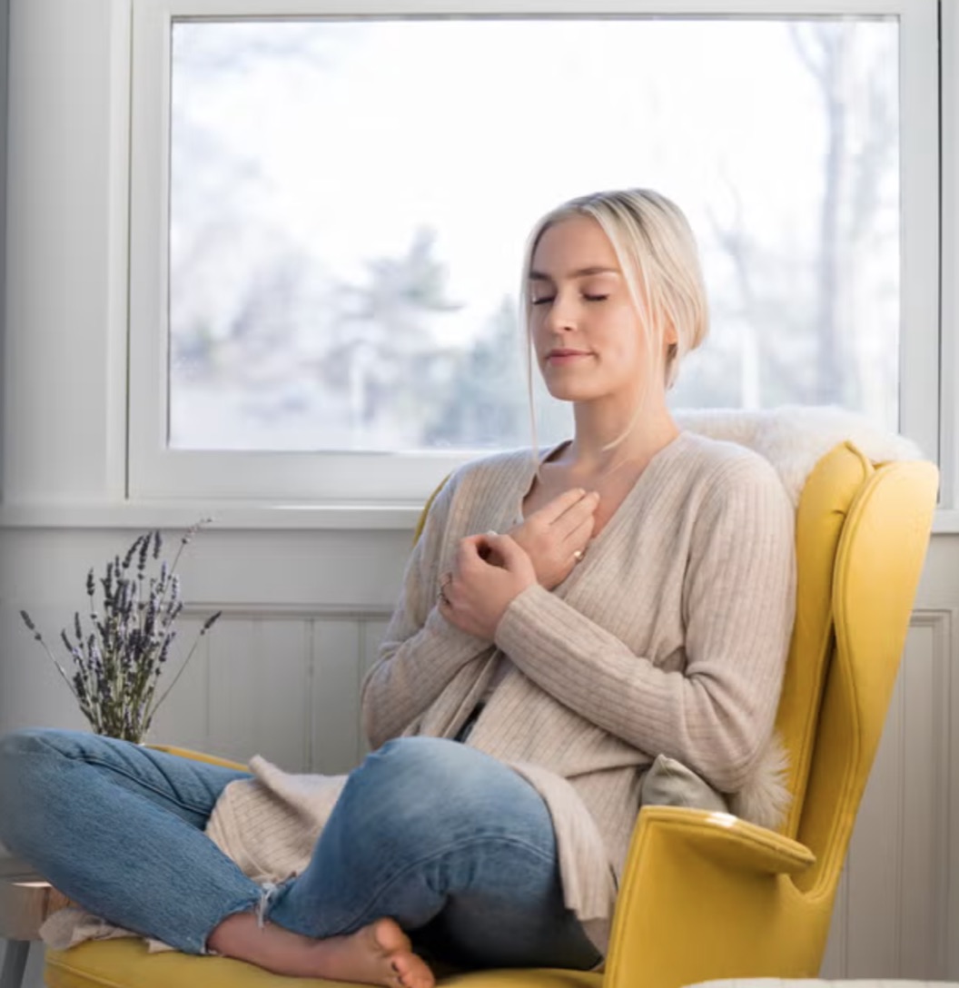 A woman resting in a chair at home by a bright window during recovery